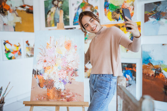 asian female artist taking picture of her own painting using smartphone