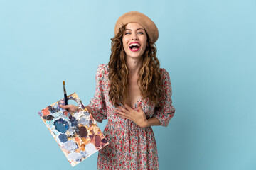 Young artist girl holding a palette isolated on blue background smiling a lot