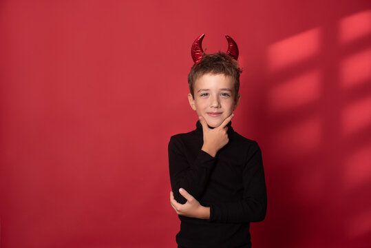 Halloween Happy child laughs out loud with devilish horns in a black turtleneck against a red studio background. Happy Halloween holidays concept.