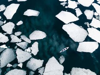 Kayak sailing between ice floes on the lake. Aerial drone view. Abstract nature background. Baikal lake, Siberia, Russia