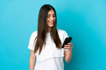 Young caucasian woman isolated on blue background sending a message or email with the mobile