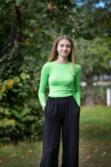 Portrait of a young beautiful blonde girl in a yellow-green blouse in the park.