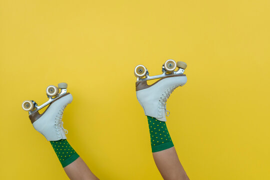 Woman legs wearing retro quad roller skates on yellow background