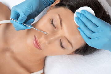 A procedure for cleansing the skin of the face from blackheads and acne. Cosmetologist treats problematic skin of a young woman's face in a beauty salon. Aesthetic cosmetology and makeup concept.