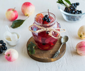 Apple jam with apple pieces and chokeberry in a jar on a light concrete background. Jam recipes.