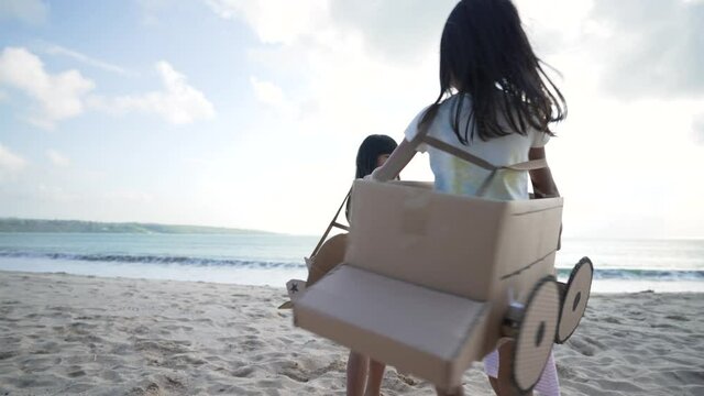 sibling and girl friend playing with cardboard airplane and car on the beach