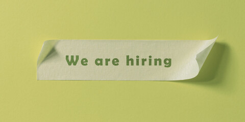 Words We are hiring written on piece of masking tape stuck to green paper background.