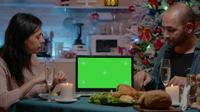 Couple eating festive meal watching horizontal green screen on laptop. Man and woman enjoying christmas eve dinner, having chroma key with mockup background and isolated template