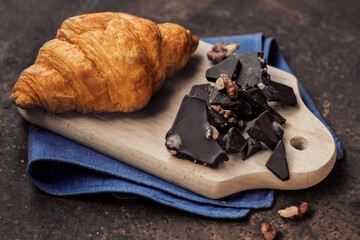 Croissant and dark chocolate with nuts on a wooden board on a rusty background. Close-up. 