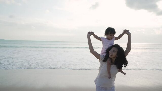 mother carrying her daughter on shoulders at the beach