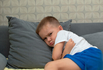 A dramatic portrait of a sad, offended little boy sitting on the couch. An unhappy child, sitting...