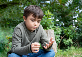 Emotional portrait of Lonely kid sitting alone on grass in the garden, Sad childplaying with leaves...