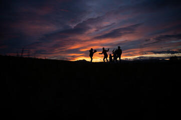 Silhouette of a family playing with a ball outside on a hill at sunset