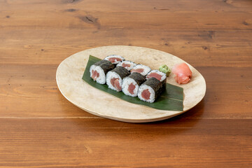 Fototapeta na wymiar Delicious red tuna maki sushi with Japanese rice and nori seaweed on banana leaf on wooden table