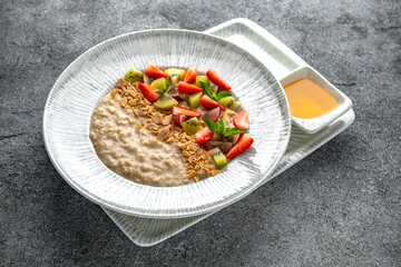 Oatmeal with condensed milk with peanuts, berries, fruits and nuts and strawberry puree. Ready menu for the restaurant. Neutral gray blue textured background