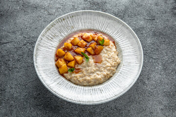 Oatmeal in milk with caramelized peach. Ready menu for the restaurant. Neutral gray blue textured background