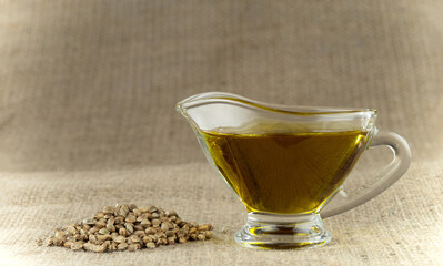 Hemp oil in a glass gravy boat with a bunch of marijuana seeds on a background of burlap.