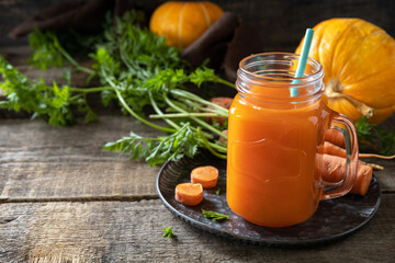 Fresh natural mixed juice, healthy food concept. Glass jar of fresh carrot juice with fresh carrots and pumpkin on a wooden rustic table. Copy space.