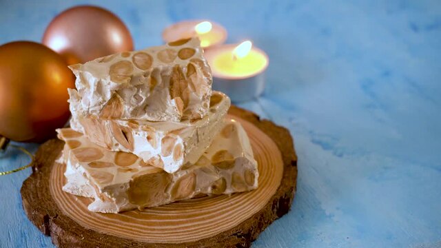 Pieces of nougat with almonds, on a blue background and Christmas decoration, with an unfocused background 