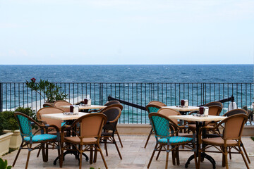 empty tables and chairs of the summer restaurant on the background of the sea horizon, outdoor cafe...