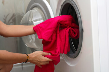 hands of a young girl put clothes in the washing machine drum