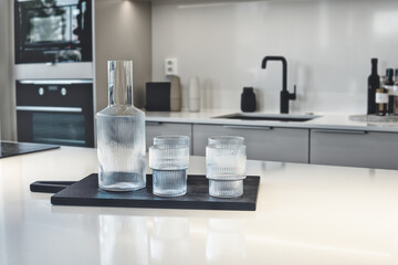 Four drinking glasses and a jug on the white kitchen table. Modern Scandinavian kitchen interior.