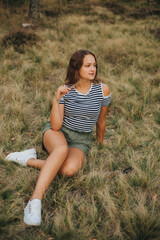 Beautiful young girl lying on the dry grass. Girl in a striped T-shirt and shorts. Portrait of a girl in the woods in nature on a beige background