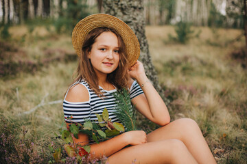Beautiful young girl lying on the dry grass. Girl in a striped T-shirt and shorts. Portrait of a girl in the woods in nature on a beige background