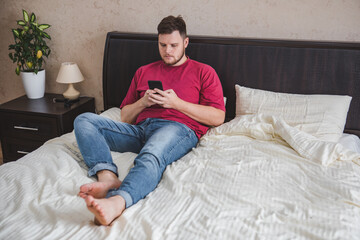 Fototapeta premium man sitting in bed surfing internet on the phone