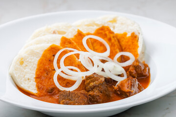 beef goulash with dumplings and rings of white onion