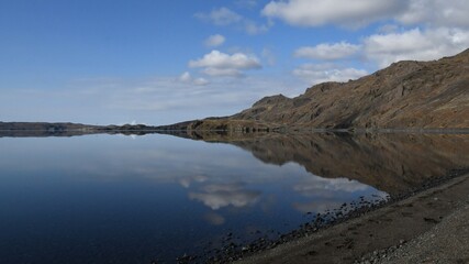 Lake Kleifarvatn in Iceland. Perfectly calm water with reflection of the mountains and sky. Blue sky in the background with white clouds.
