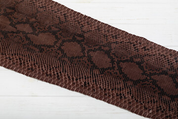 Brown dyed folded natural genuine python leather on the wooden table	
