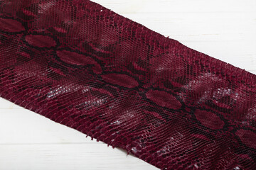 burgundy dyed genuine natural python leather  on the wooden table	
