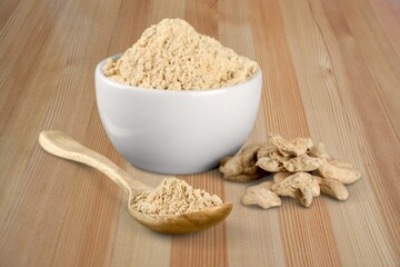 Turmeric powder in the bowl and root on the desk