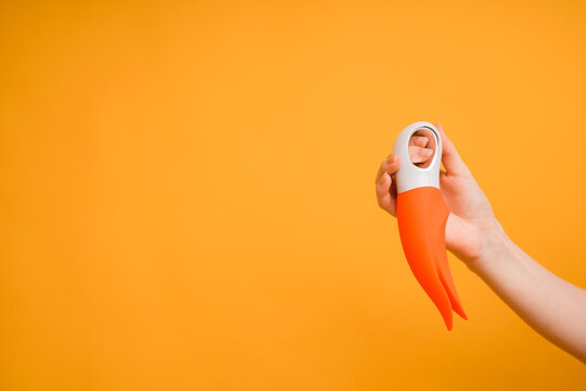 A woman's hand holds a red dildo or vibrator for sex on a yellow background.Useful for a sex shop