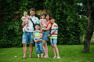 Beautiful large family with young parents and four kids stand in green grass at courtyard.