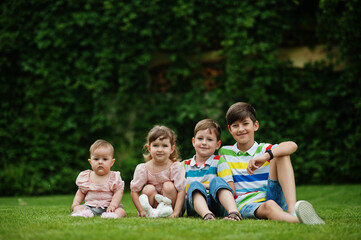 Beautiful large family with four kids sitting in green grass at courtyard.