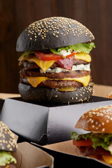 Big grilled beef burgers on a cardboard box on a dark background, side view. Takeaway hamburger. Burger in the box, fast food.