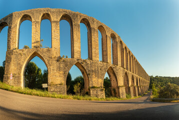 Panoramic view of the Pegões Aqueduct, near the city of Tomar in Portugal, lit by the sun at the end of the day with a blue sky in the background.