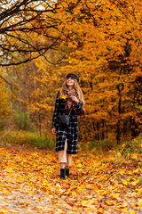 Pretty young girl in fashion clothes walks in autumn forest with colorful yellow leaves