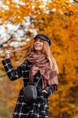 Fototapeta na wymiar Beautiful young woman with a smile in a fashionable coat with a scarf and a hat walks in an autumn park with yellow foliage