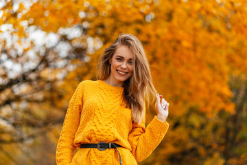 Smiling stylish happy woman with sweet smile in vintage knitted sweater walks in autumn park with golden fall leaves