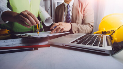 Two colleagues discussing data working and tablet, laptop with on on architectural project at construction site at desk in office