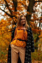 Fototapeta na wymiar Fashionable beautiful smiling girl in stylish autumn clothes is walking in a golden fall park with yellow foliage