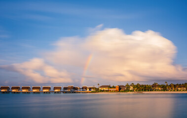 Obraz premium Island in ocean, overwater villas at the time sunset with rainbow. Crossroads Maldives, saii lagoon hotel. July 2021. Long exposure picture