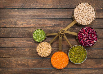 Legumes set in vintage copper scoops on wooden background with copy-space.