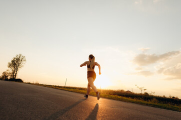 Fototapeta na wymiar Young sporty girl running on a road at sunset. Lifestyle sports motivation. 