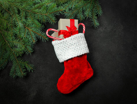 Christmas composition, red stocking with gifts and fir branches on a black background.