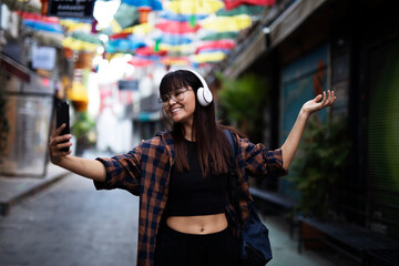 Plakat Young smiling woman outdoors. Beautiful woman listening to music while walking through the city.