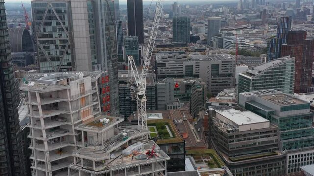 Ascending footage of crane on new skyscraper constriction site. Tall downtown buildings around. London, UK